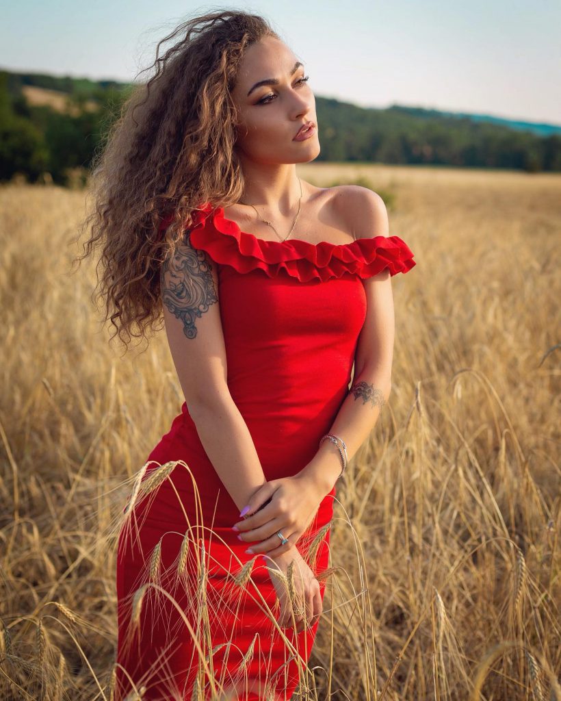 Carlotta in abito rosso in un campo di grano a Pienza Val d'Orcia