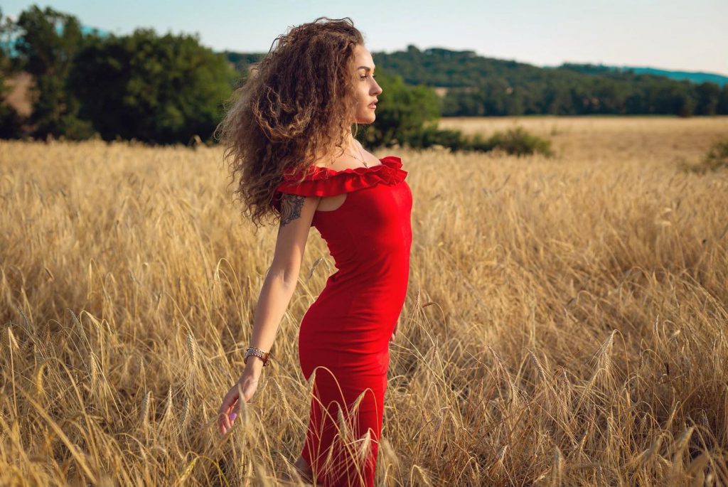 Carlotta in abito rosso in un campo di grano a Pienza Val d'Orcia