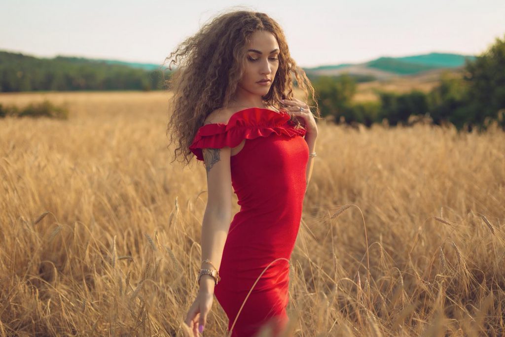 Carlotta in abito rosso in un campo di grano a Pienza Val d'Orcia