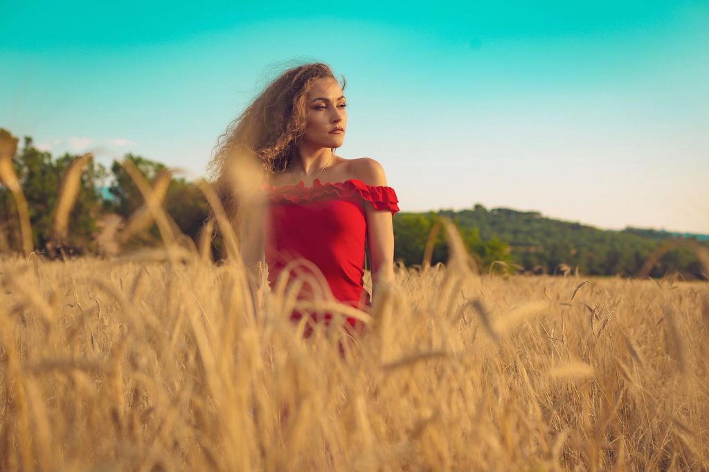 Carlotta in abito rosso in un campo di grano a Pienza Val d'Orcia