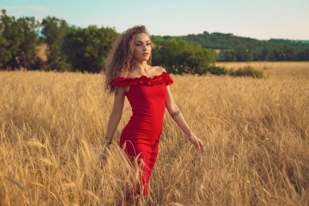 Carlotta in abito rosso in un campo di grano a Pienza Val d'Orcia