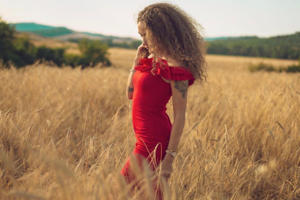 Carlotta in abito rosso in un campo di grano a Pienza Val d'Orcia