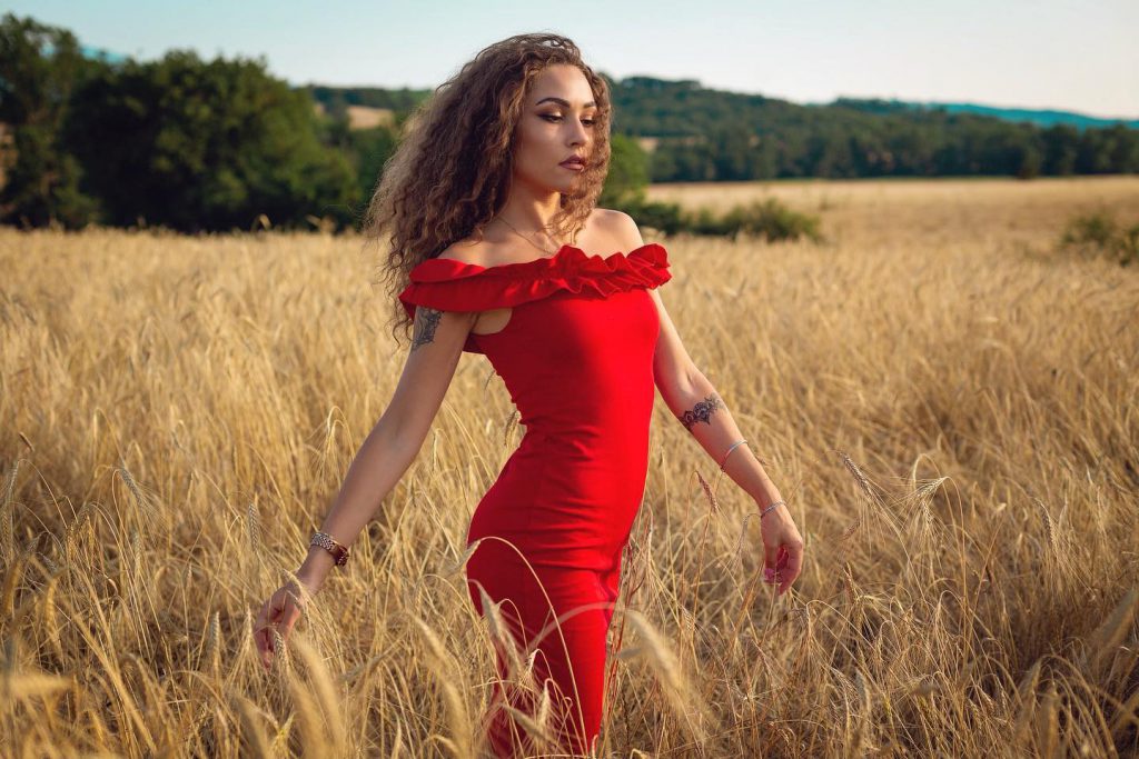 Carlotta in abito rosso in un campo di grano a Pienza Val d'Orcia